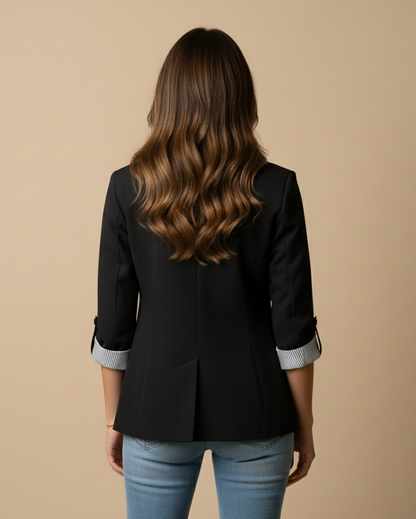 Person wearing a black blazer and light blue jeans on a beige background