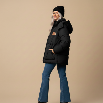 Woman wearing a black coat, black beanie, and blue jeans on a beige background